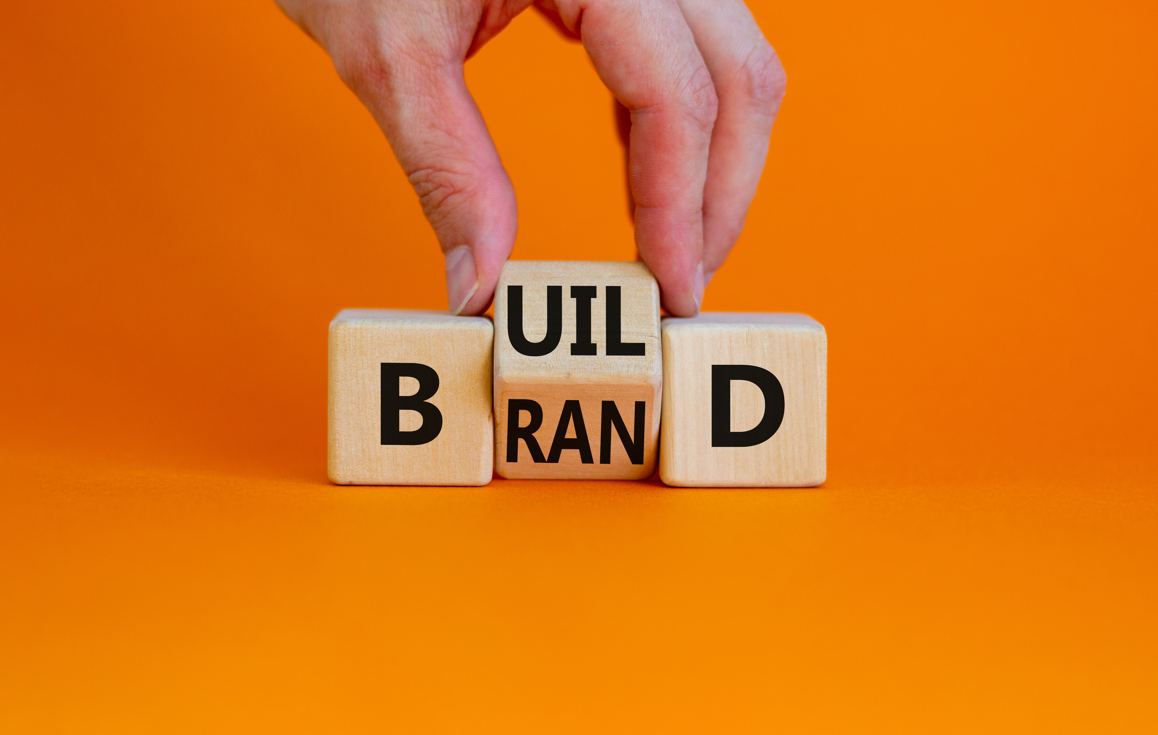 Build your brand symbol. Businessman turns wooden cubes and changes the word 'build' to 'brand'. Beautiful orange background. Build your brand and business concept. Copy space.